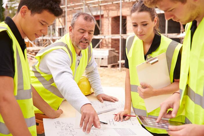 Apprentices and manager at building site reviewing blue prints