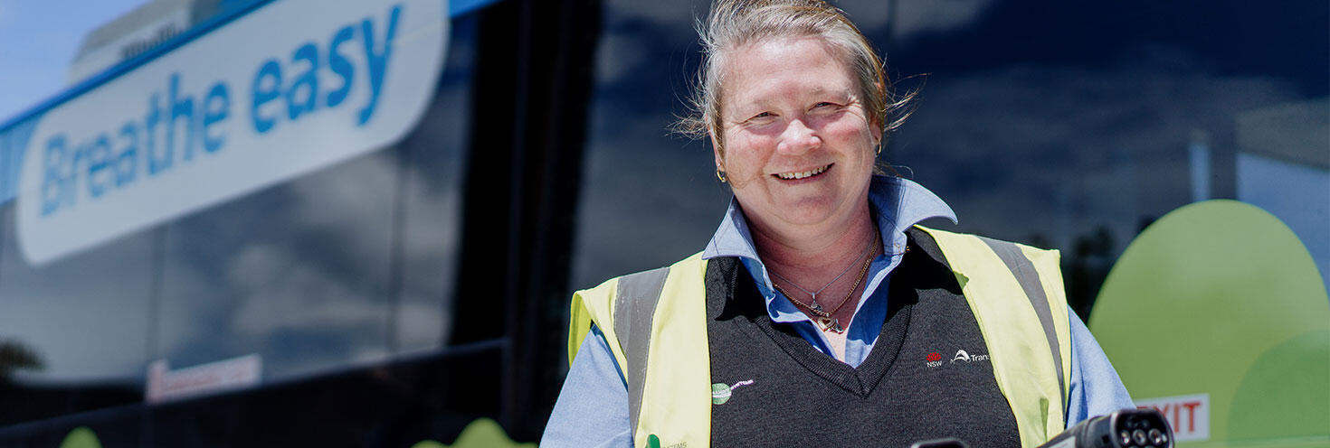 Smiling female bus driver in front of a blue zero-emission bus.